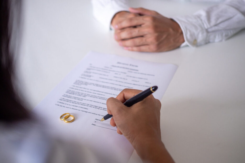 Legal document being signed by one person with another's hands in the background, representing the steps involved in determining spousal support during Iowa divorce proceedings.