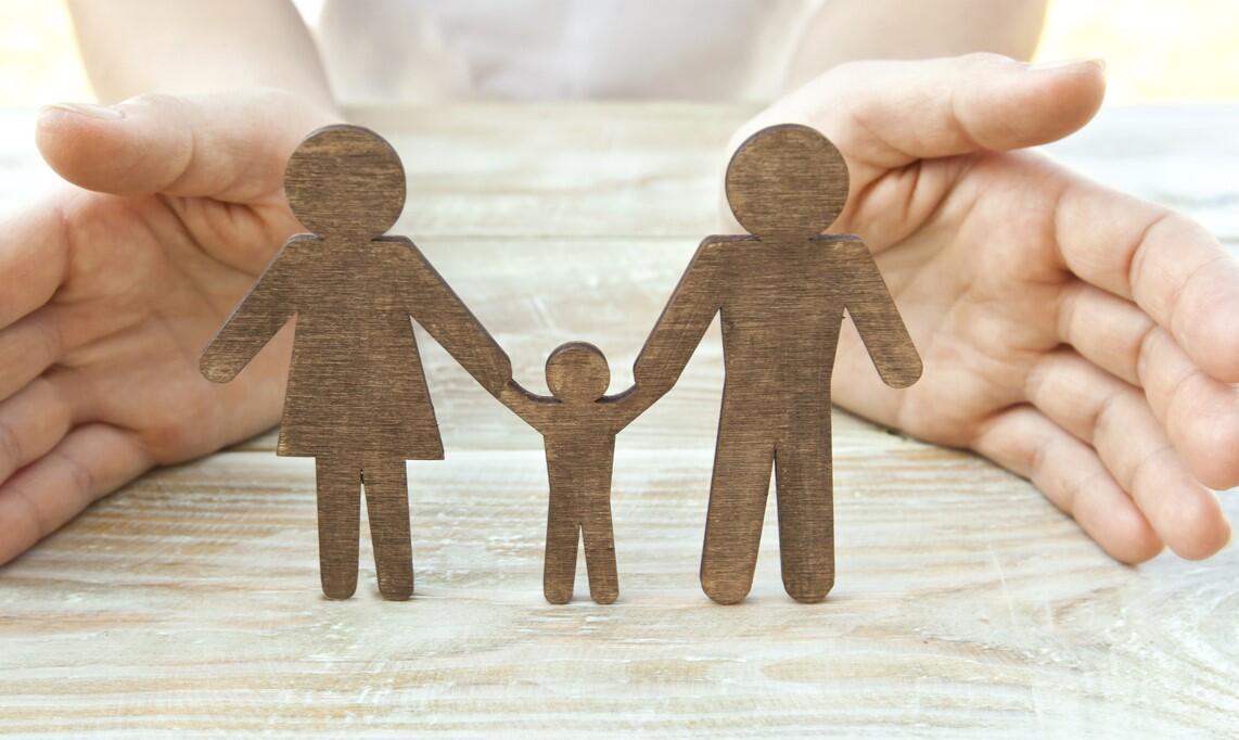 Wooden figures of a family (parents and child) protected by cupped hands, symbolizing the legal process of child custody modification in Des Moines and the need to prove a significant change in circumstances.