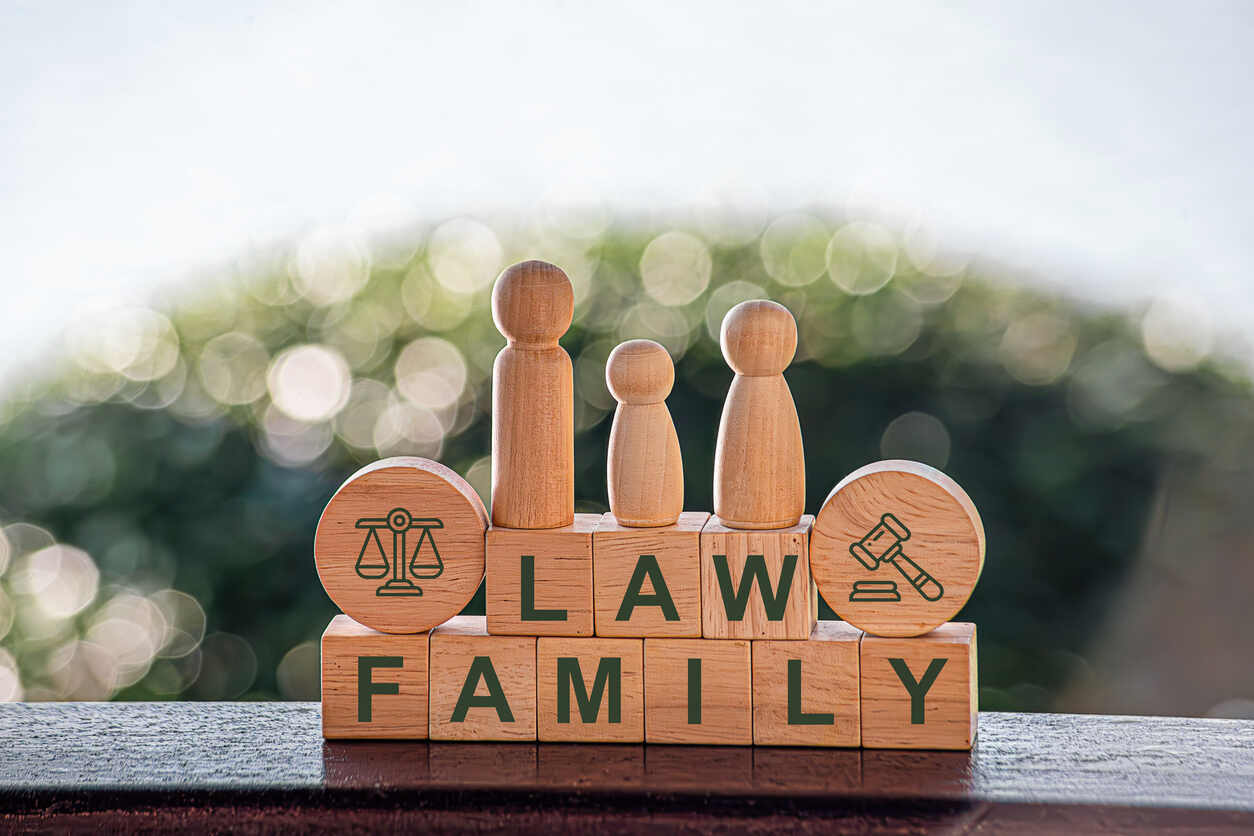 Overhead shot of hands sheltering paper family figures, next to a piggy bank and house keys, for a custody parenting plan.