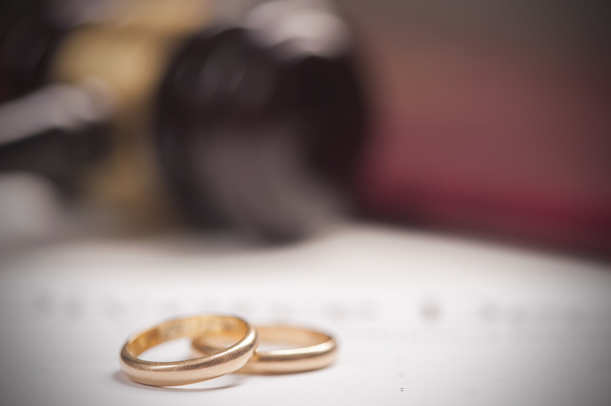 Two gold wedding rings on a white surface and in background legal papers, symbolizing prenuptial agreements in marriages.