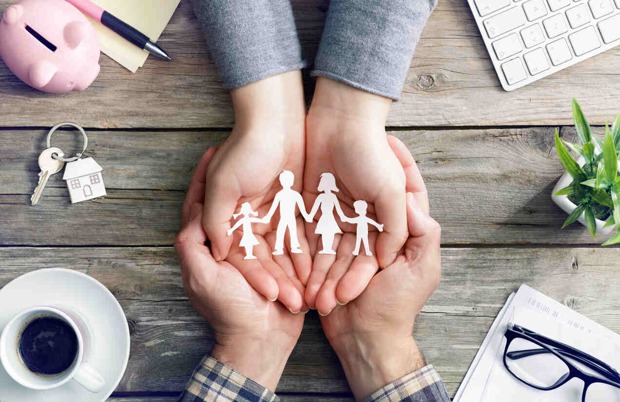 Hands holding paper cutouts of a family, surrounded by symbols of home and finance, representing a parenting plan.