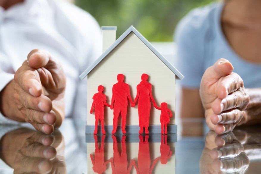 Paper cutout figures of a family holding hands in front of a house, with two hands symbolizing the division of assets during an Iowa divorce.